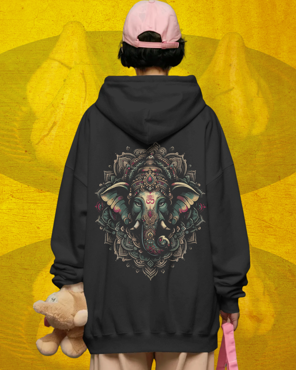 Person wearing a black hoodie with a colorful elephant design on the back, standing against a yellow background